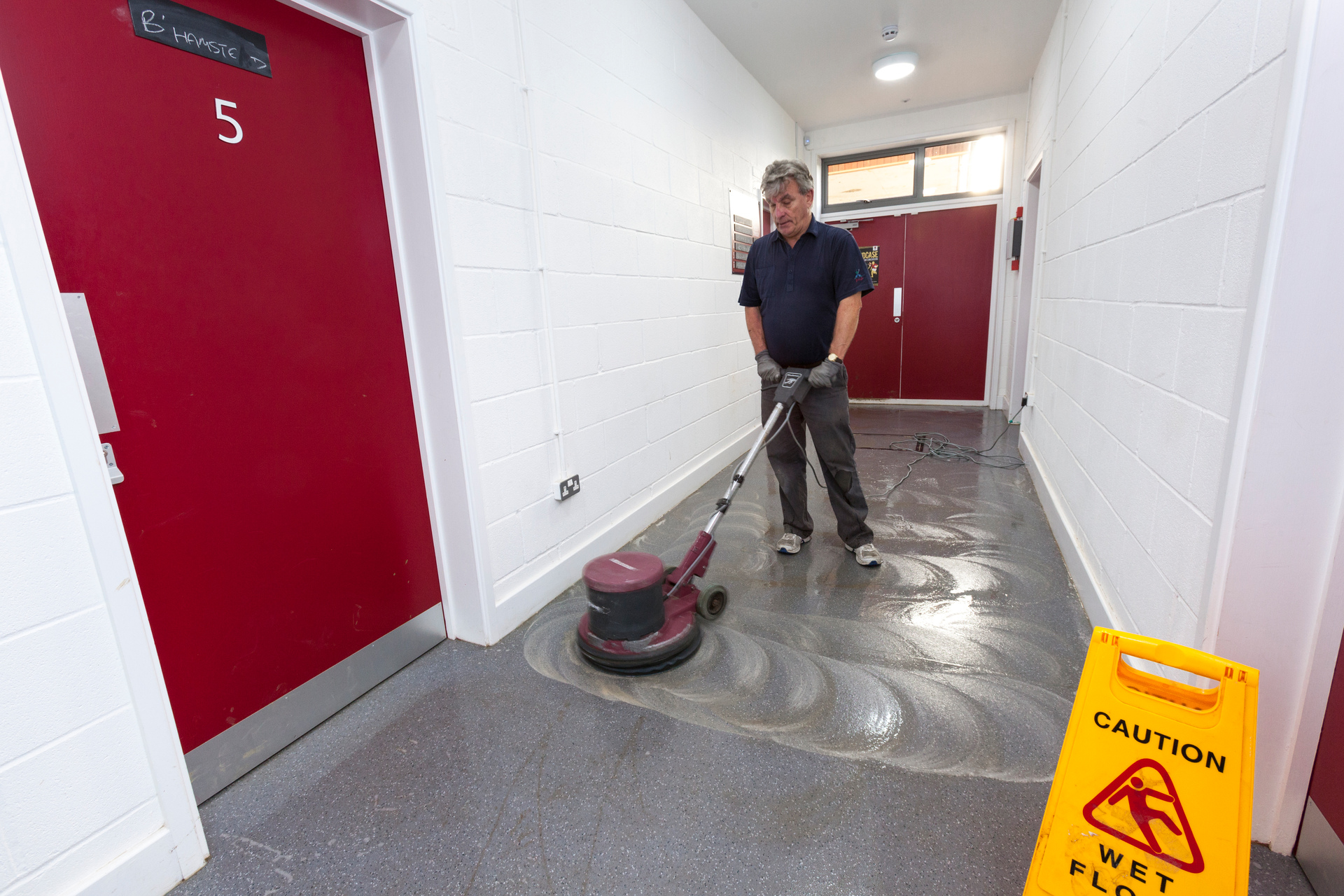 un limpiador con uniforme rojo limpia el suelo con la ayuda del